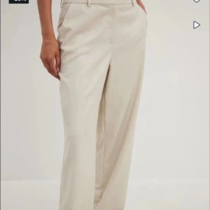 Beige kostymbyxor - Snygga beige kostymbyxor i normal passform. Perfekta för både kontoret och mer avslappnade tillfällen. De har en klassisk design med  raka ben, vilket ger en stilren look. Materialet är mjukt och bekvämt, vilket gör dem sköna att bära hela dagen.