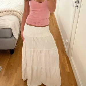 Vit långkjol från Lager 157 - Säljer en vit långkjol från Lager 157 med smock i midjan och flera volanger. Kjolen är luftig och har en avslappnad passform, perfekt för varma dagar. Tillverkad i ett mjukt och lätt material som känns skönt mot huden.🤗