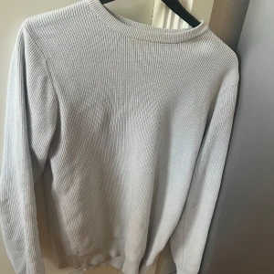 Ljusgrå stickad tröja från S.C.W - Säljer en stilren ljusgrå stickad tröja från S.C.W i storlek S. Tröjan har rund halsringning och långa ärmar, perfekt för lager-på-lager. Enkel och klassisk design som passar till det mesta.