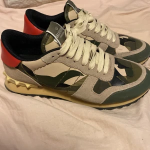 Valentino Rockrunner  - Säljer ett par Valentino Rockrunner sneakers med beige och gröna camouflagepaneler, röda detaljer på hälen och krämfärgade snören. Skorna har en unik nitat detalj på sulan och är tillverkade i en mix av mocka och skinn. Låda finns inte. Pris är inte hugget i sten 