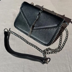 Svart handväska - Säljer denna svarta handväska! Väskan kan bäras som antingen axelväska eller handväska då man kan ställa in bandet hur man vill! Väskan har dragkedja och två fack i  sig. Spelkort för storleksreferens! Väskan är använd 1 gång så väldigt sparsamt använd och inga tecken på slitage🩵 