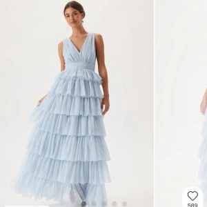 Oanvänd balklänning - Drömmig ljusblå långklänning med flera lager volanger i tyll. Djup v-ringning fram och öppen rygg med breda axelband. Perfekt för bal eller festliga tillfällen. Storlek 38, passar bra för en vanlig S/M.