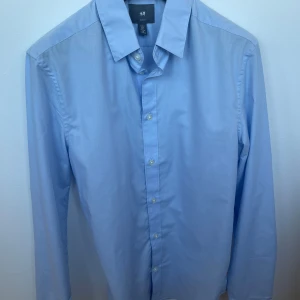 Ljusblå skjorta från H&M - Klassisk ljusblå skjorta från H&M med lång ärm och knappar framtill. Knappt använd och i mycket bra skick! 