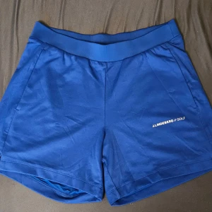 Blå shorts från J.Lindeberg - Snygga blå shorts från J.Lindeberg med elastisk midja och diskret logga på ena benet. Perfekta för golf eller andra sportiga aktiviteter. Tillverkade i ett mjukt och lätt material som känns skönt mot huden.
