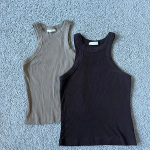 Två ribbade linnetoppar i beige och brunt - Säljer två ribbade linnetoppar i klassisk modell, en i beige och en i brunt. Båda har rund halsringning och ärmlöst snitt, perfekta för varma dagar eller som lager under andra plagg. Den bruna toppen är st S och den beige st XS🌸🌸