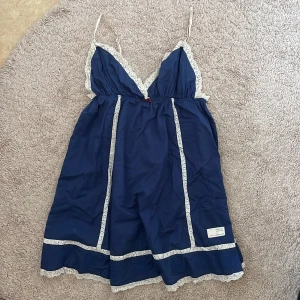 Marinblå spetsklänning från Odd Molly - Passar S/M, Söt marinblå klänning från Odd Molly med vita spetsdetaljer längs kanterna och smala axelband. Djup v-ringning och liten rosett framtill. Klänningen har broderad detalj på ryggen och är kort i modellen. Den är jättesöt och är väldigt fin i bysten<3