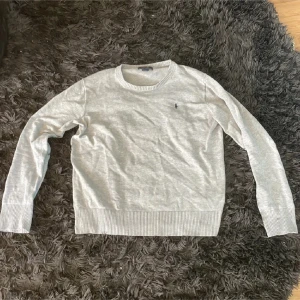 Ljusgrå tröja från Polo Ralph Lauren - Säljer en ljusgrå tröja från Polo Ralph Lauren med rund halsringning och diskret broderad logga på bröstet. Tröjan har långa ärmar och ribbade muddar vid ärmslut och nederkant. Perfekt för en stilren och klassisk look.