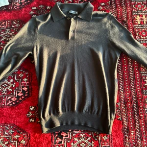 Svart merinoull pikétröja från Mango - Säljer en klassisk svart pikétröja i mjuk merinoull från Mango. Tröjan har lång ärm, krage och knäppning med två knappar framtill. Nytt skick, aldrig använd