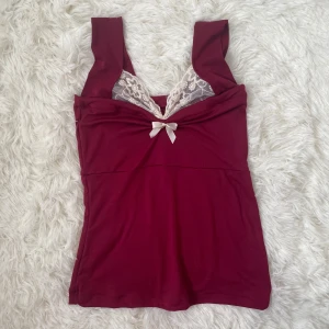 Vinröd linnetopp med spets och rosett från lovemelinna (Instagram) - Supersöt vinröd linnetopp med breda axelband, vit spetsdetalj vid bysten och en liten rosett framtill. Handmade av en small business som heter lovemelinna på Instagram. Ny pris ca 500kr + tullavgift +utlänskt leverans = ca 850kr. Är i nyskick och ligger fortfarande i original kartong. Väldigt små, för de som har byst under 78cm och midjan under 60cm.