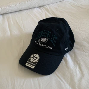 Svart keps från '47 Super Bowl LII Champions - Svart keps från märket '47 med broderad text 'Super Bowl LII Champions' och Philadelphia Eagles-logga framtill. Justerbar passform med böjd skärm och broderad logga på sidan.