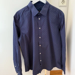 Ny Mörkblå skjorta med mönster - Mörkblå skjorta med mönster som aldrig var använd, endast tvättad.  Skjortan har långa ärmar och knappar framtill. Storlek L.