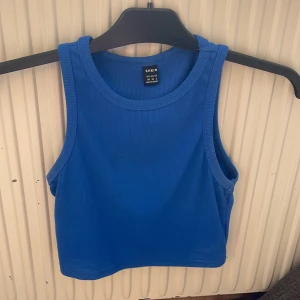 Blå ribbad croppad linnetopp från SHEIN - Säljer en blå croppad linnetopp från SHEIN i ribbat material. Toppen är ärmlös med rund halsringning och har en tight passform. Perfekt för varma dagar eller som ett lager under en skjorta.