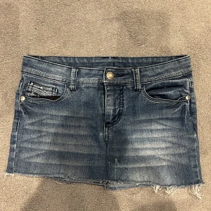 Jeanskjol med rå kant och dekorerade bakfickor - Säljer en blå jeanskjol med rå, fransad nederkant och snygga dekorationer på bakfickorna. Har sytt om den från jeans shorts till jeans kjol. Midjemått=34cm, Längd=27cm
