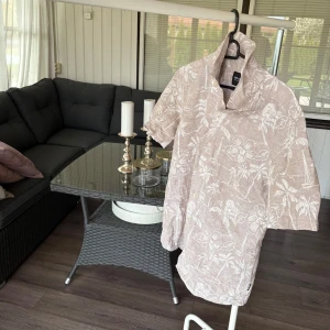 Beige kortärmad skjorta med blommigt mönster från ONLY & SONS - Säljer en beige kortärmad skjorta från ONLY & SONS med diskret blommigt mönster. Skjortan har klassisk krage och knäppning framtill. Perfekt för varma dagar när du vill ha en avslappnad men snygg stil. Köparen står för frakt🤩