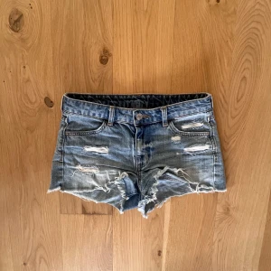 lågmidjade jeansshorts med slitningar från H&M - Säljer ett par blå jeansshorts från H&M med råa kanter och flera slitningar framtill och på bakfickan. 