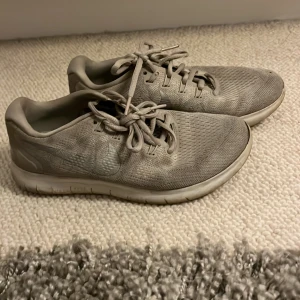 Grå Nike sneakers i mesh, stl 37.5 - Säljer ett par grå Nike sneakers i storlek 37.5. Skorna har en luftig ovandel i mesh, klassisk Nike-logga på sidan och snörning framtill. Perfekta för dig som gillar sportig stil och vill ha bekväma skor till vardagen.