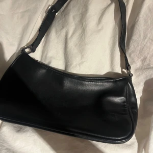 Svart axelväska i skinnlook - Snygg svart axelväska med justerbart axelband. Väskan är från monki och är nästintill aldrig använd, den är liten med rymlig 