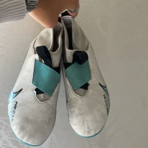 Nike Mercurial Air Zoom fotbollsskor - Säljer ett par Nike Mercurial Air Zoom fotbollsskor i vitt med blå och rosa detaljer. Skorna har en strömlinjeformad design, täckt snörning och mönstrad sula med dobbar för gräsplan. Swoosh-logga på sidan och Mercurial-tryck bak. Perfekt för dig som vill ha speed och kontroll på planen. ABS! Pris går att diskutera!