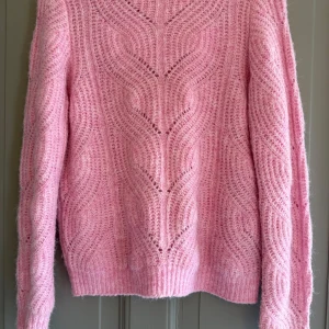 Rosa stickad tröja med mönster - Supermysig rosa stickad tröja med snyggt strukturerat mönster och ribbade muddar. Tröjan har lång ärm och är fluffig och mjuk, perfekt för kyliga dagar. Passar dig som gillar färg och vill ha en cozy vibe i garderoben.