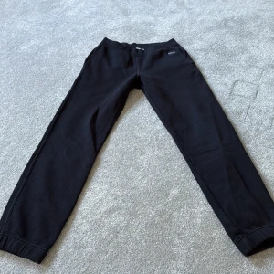 Svarta mjukisbyxor från Hugo Boss - Svarta mjukisbyxor från Hugo Boss med broderad logga på fickan. Byxorna har resår i midjan och vid bensluten, samt sidofickor. Perfekta för chill eller träning, tillverkade i mjukt bomullsmaterial.
