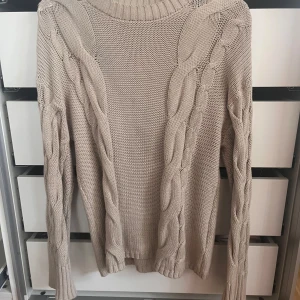 Beige stickad tröja från lager 157 XS - Säljer en beige stickad tröja från lager 157 i storlek XS. Tröjan har grova flätstickade detaljer längs ärmar och sidor, rund hals och långa ärmar. Perfekt för dig som gillar en chill och mysig stil med snygga detaljer.