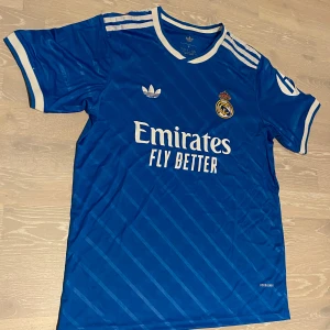 Blå Real Madrid 25-26 T-shirt  - •Säljer en jätte fin 25-26 blå Real Madrid T-shirt.  •Den är inte använd bara testad, jätte bra skick och inga fläckar eller hål.  •Och det är storlek M och måtten finns på dem sista bilderna •Priset kan diskuteras och skickar inom 24 Tim 💨😊