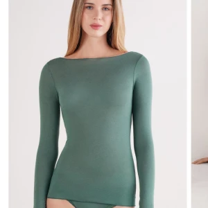 Grön långärmad topp med båtringning - Snygg grön långärmad topp med båtringning och figurnära passform. Enkel och stilren design som passar perfekt till jeans eller kjol. Mjuk och stretchig känsla för en bekväm look.
