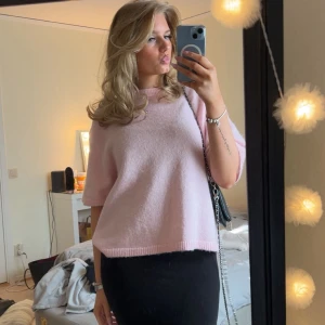 Ljusrosa stickad tröja från Gina Tricot - Superfin ljusrosa stickad tröja från Gina Tricot med korta ärmar och rund hals. Tröjan har en loose passform och ribbade kanter vid ärmslut, hals och nederkant. Använd några få gånger bara.Perfekt att styla med kjol eller jeans för en chill look.