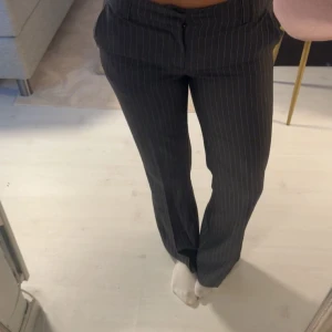 Svarta/mörkgrå kostymbyxor med smala ränder - Snygga svart/grå kostymbyxor med tunna vita ränder. Byxorna har normal passform, raka ben och klassiska fickor fram. Perfekta för en clean och stilren look. Midjan är midwaist och materialet känns som bomull eller polyester. Jag är 170cm lång