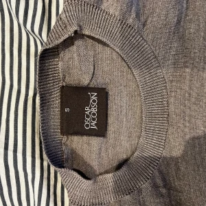 Grå stickad tröja från Oscar Jacobson - Snygg grå stickad tröja från Oscar Jacobson i storlek S. Tröjan har rund halsringning och långa ärmar med ribbade muddar. Perfekt för dig som gillar stilrena och klassiska plagg med en modern touch. Materialet är mjukt och tunt, vilket gör den skön att bära. Ändå defekten är en liten tråd som sticker ut på armen men inget synligt förutom om man kollar nära! Annars riktigt fräsch!😀😀