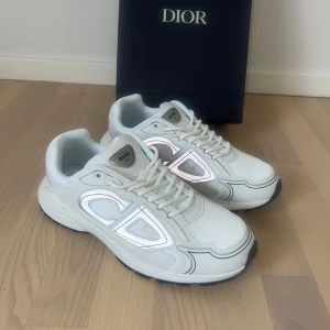 B30 - Snygga vita B30 med reflekterande CD-detaljer på sidorna. Skorna har en chunky sula i vitt och svart, meshpaneler för extra andningsförmåga och klassisk snörning. Perfekta för dig som vill sticka ut med exklusiv style.