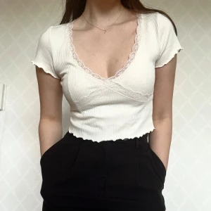 Vit topp med spets - Supersöt vit croppad topp med ribbad struktur och v-ringning. Toppen har spetsdetaljer längs urringningen🥰 