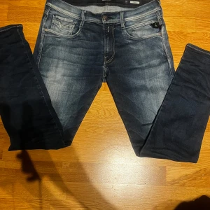 Replay Anbass jeans i mörkblå denim 32/32 - Snygga Replay Anbass jeans i mörkblå tvätt med slitningar och ljusare partier. Klassisk femficksmodell med broderade bakfickor och Replay-logga på myntfickan. Jeansen har smal passform och är tillverkade i stretchig bomullsdenim för extra komfort.