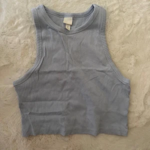 Ljusblå ribbad linnetopp från H&M - Säljer en ljusblå croppad linnetopp från H&M i storlek L. Toppen är ribbad och har breda axelband samt rund halsringning. Perfekt för varma dagar och enkel att matcha med jeans eller shorts.