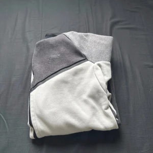 Nike hoodie i grå och vit fleece - Säljer en snygg hoodie från Nike i olika grå nyanser och vitt. Tröjan har en modern design med paneler och är tillverkad i mjuk fleece som är perfekt för kyliga dagar. Diskret Nike-logga på bröstet och klassisk huva för extra komfort.