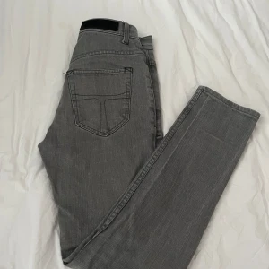 Grå jeans från Tiger of Sweden - Snygga grå jeans från Tiger of Sweden med klassisk femficksdesign och raka ben. Jeansen har en stilren look med diskreta sömmar och metallknapp framtill. Perfekta för dig som gillar en clean och enkel stil Priset kan diskuteras. 