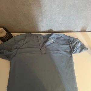  Buy one get one free - Snygg blå t-shirt med korta ärmar och en stilren knappdetalj vid halsen. T-shirten har en enkel design med sömmar över axlarna och är perfekt för dig som gillar en clean och chill look. Passar dig som vill ha någo