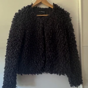 Svart teddyjacka från KappAhl - Mysig svart teddyjacka från KappAhl i storlek S. Jackan har en fluffig och lockig yta som ger en cool och trendig look. Perfekt för dig som vill sticka ut och hålla dig varm under kyliga dagar. Enkel att matcha med både jeans och kjol. Använd en gång. Jackan har en knäppning upptill.