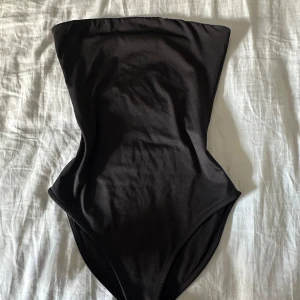 Svart bandeau body från Bikbok - Snygg svart bandeau body från Bikbok i storlek XS. Stilren och enkel design utan axelband, perfekt för dig som vill ha en klassisk look. Materialet är mjukt och följsamt syntet som sitter bekvämt mot kroppen.