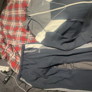 Blå och grå dress från BOSS - Säljer en snygg tracksiut från BOSS i mörkblått och grått med vita detaljer. Dressen har elastisk midja med dragsko och sidofickor. Perfekta för chill eller träning, riktigt sköna och stilrena med sportig vibe.   Köpt för 3400