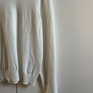 Vit stickad tröja från H&M - Säljer en enkel och stilren vit stickad tröja från H&M i storlek L. Tröjan har långärmade ärmar och ribbade muddar vid ärmslut och nederkant. Perfekt för lager-på-lager och passar till jeans eller kjol. Mjuk och skön känsla.