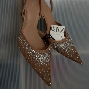 Glittriga pumps med spetsig tå från Zara - Snygga beige pumps från Zara med spetsig tå och hög klack. Skorna är täckta med glittrande stenar framtill och har en elegant meshdetalj. Perfekta för dig som vill sticka ut med en glamorös look. Helt nya med prislappar på✨