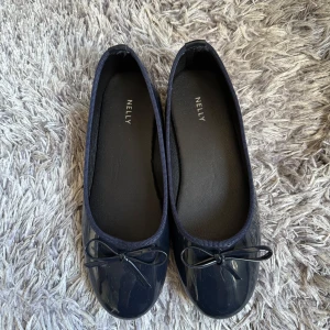 Mörkblå ballerinaskor från Nelly - Snygga mörkblå ballerinaskor från Nelly med glansig finish och söt rosettdetalj framtill. Skorna har rund tå och är perfekta för en stilren och enkel look. Passar till både jeans och klänning. Aldrig använda. Ny pris 179 kr