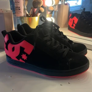 Svarta DC sneakers med rosa detaljer - Säljer ett par svarta DC sneakers med stora rosa DC-loggor på sidorna och rosa detaljer på sulan. Skorna har snörning och en klassisk, rund tå. Det är använda runt 5 gånger och köptes för 1000 för cirka ett halv år sen. Fräscha som nya