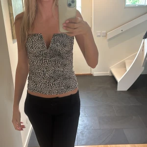Leopardmönstrad tubtopp med v-ringning - Snygg tubtopp med leopardmönster i svart och beige. Toppen har en cool v-ringning framtill och sitter tight mot kroppen. Perfekt för dig som vill sticka ut lite extra med ett trendigt djurmönster💗💗.