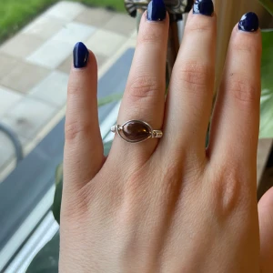 Silverring med brun sten ”sötvattenpärla” - Unik handgjord ring i silverfärgad metall med en oval, brun sten i mitten. Ringen har en stilren design med tråddetaljer runt stenen. Perfekt för dig som vill ha något speciellt till din accessoarsamling.