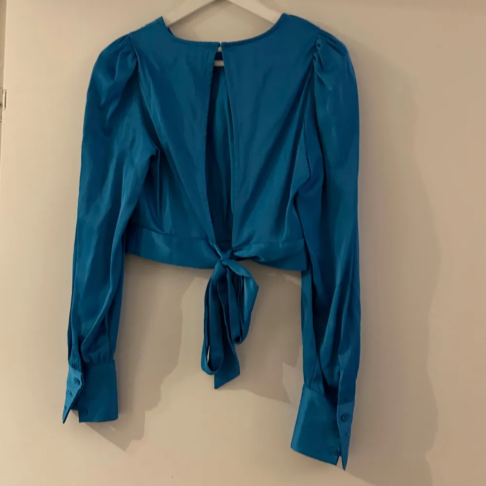 Blå blus som man kan knyta i ryggen. . Puserot.