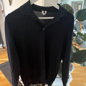 Mörkblå långärmad pikétröja - Säljer en mörkblå långärmad pikétröja i storlek S från Arket. Tröjan har klassisk krage och knäppning framtill, perfekt för en stilren och enkel look. Passar bra till både jeans och kostymbyxor.