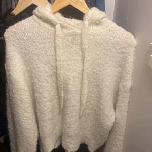 Vit fluffig hoodie från H&M Divided - Mysig vit hoodie från H&M Divided i fluffigt material. Tröjan har huva och dragsko samt långa ärmar. Perfekt för kyliga dagar när du vill vara både bekväm och snygg.