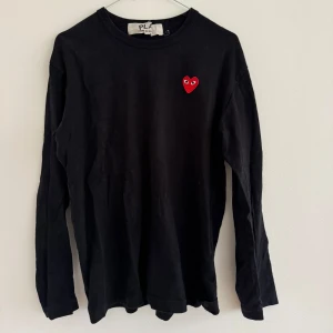 Svart långärmad tröja från Comme des Garçons Play - Svart långärmad tröja från Comme des Garçons Play med det ikoniska röda hjärtat broderat på bröstet. Enkel och stilren design i mjuk bomull, perfekt för alla tillfällen. Sparsamt använd! Lika snygg på kille som tjej! 